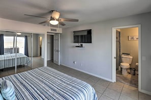 Ein Schlafzimmer mit Bett, Deckenventilator, Fernseher und einem durchgehenden Türrahmen sichtbaren Badezimmer.