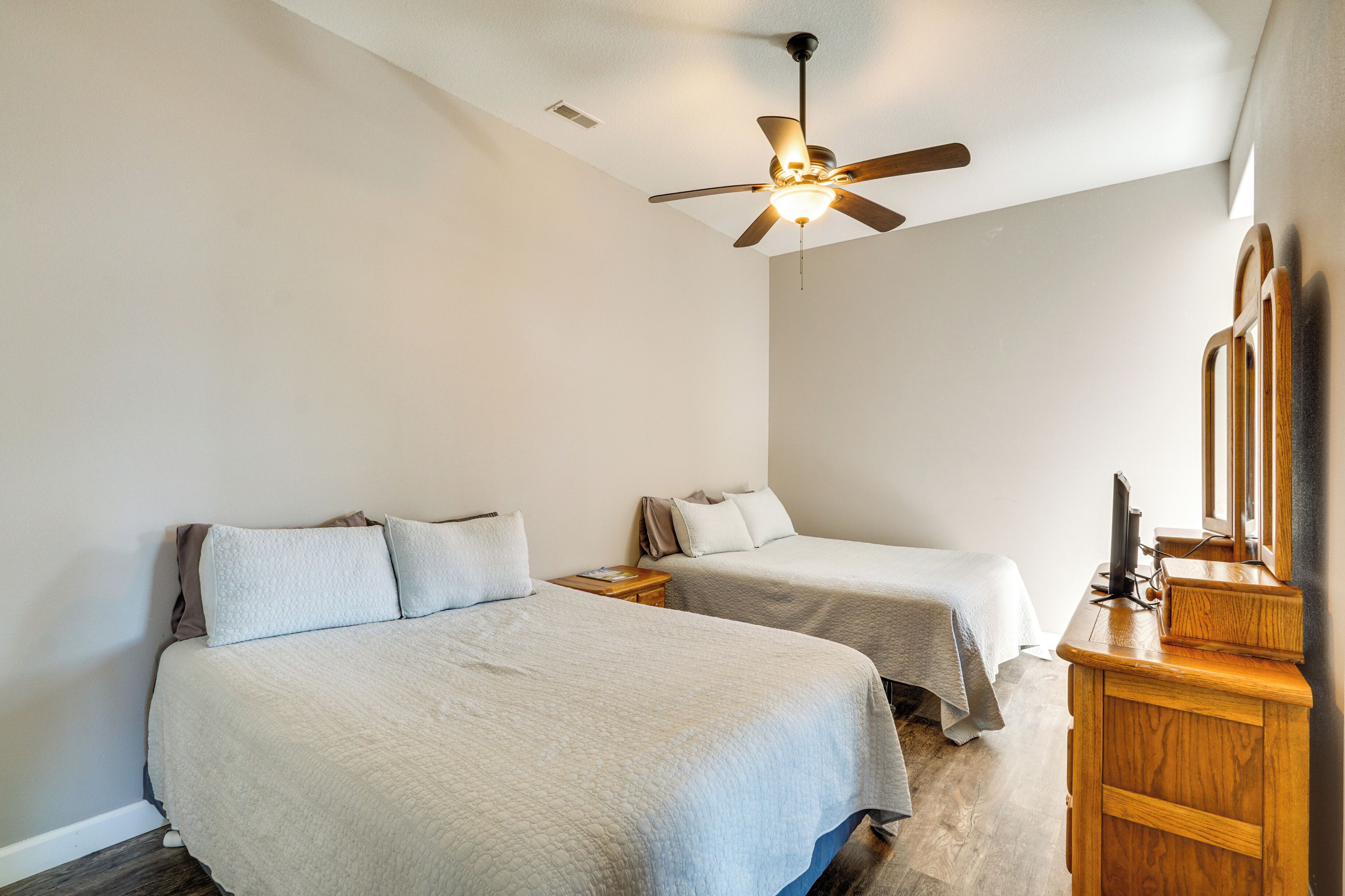 A bedroom with two beds, a ceiling fan, a wooden dresser, and a mirror.