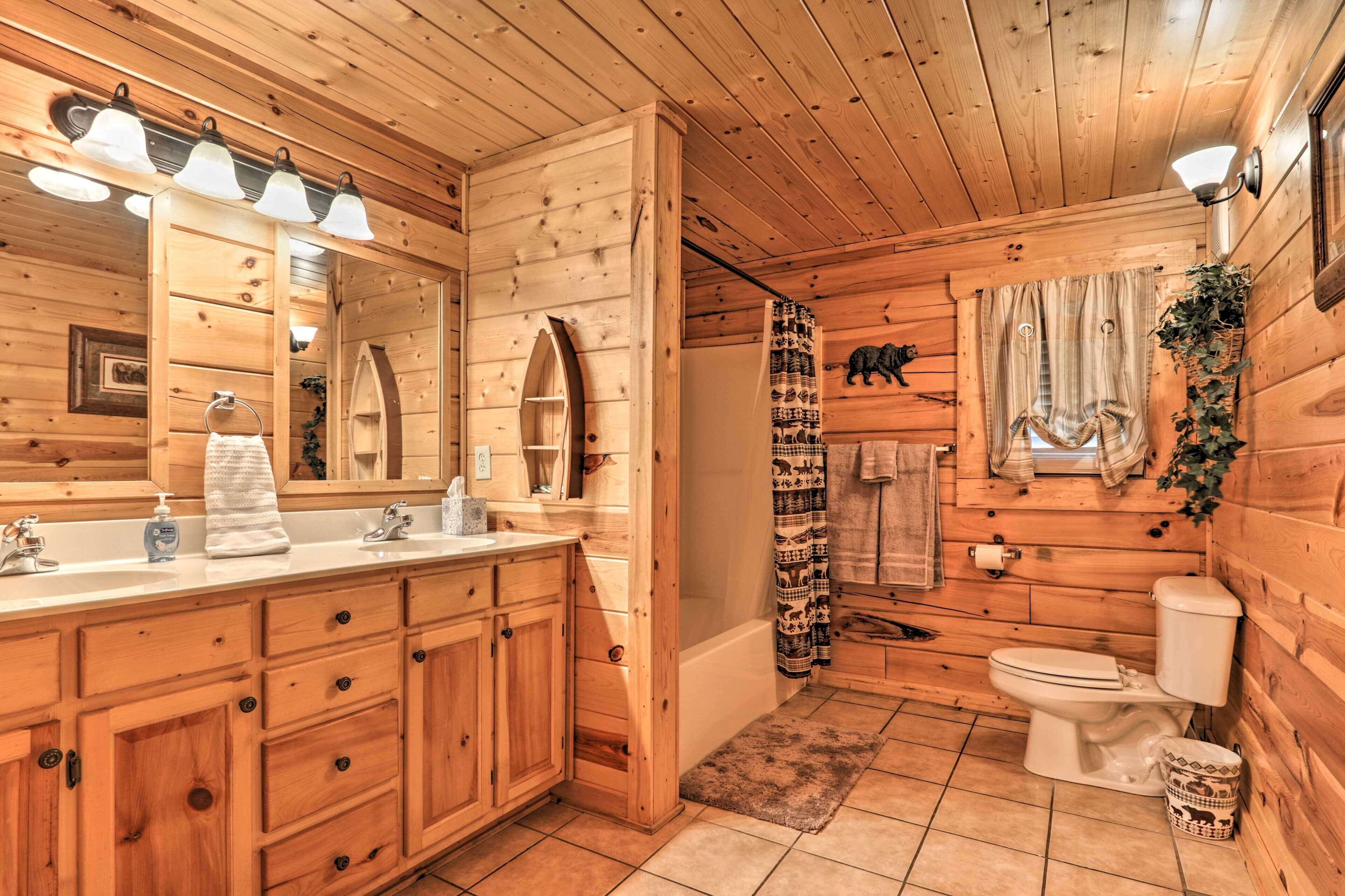 Une salle de bain rustique, avec des murs en bois, un meuble-lavabo en bois, un grand miroir, un rideau de douche, des toilettes et un lavabo équipé de distributeurs de savon.
