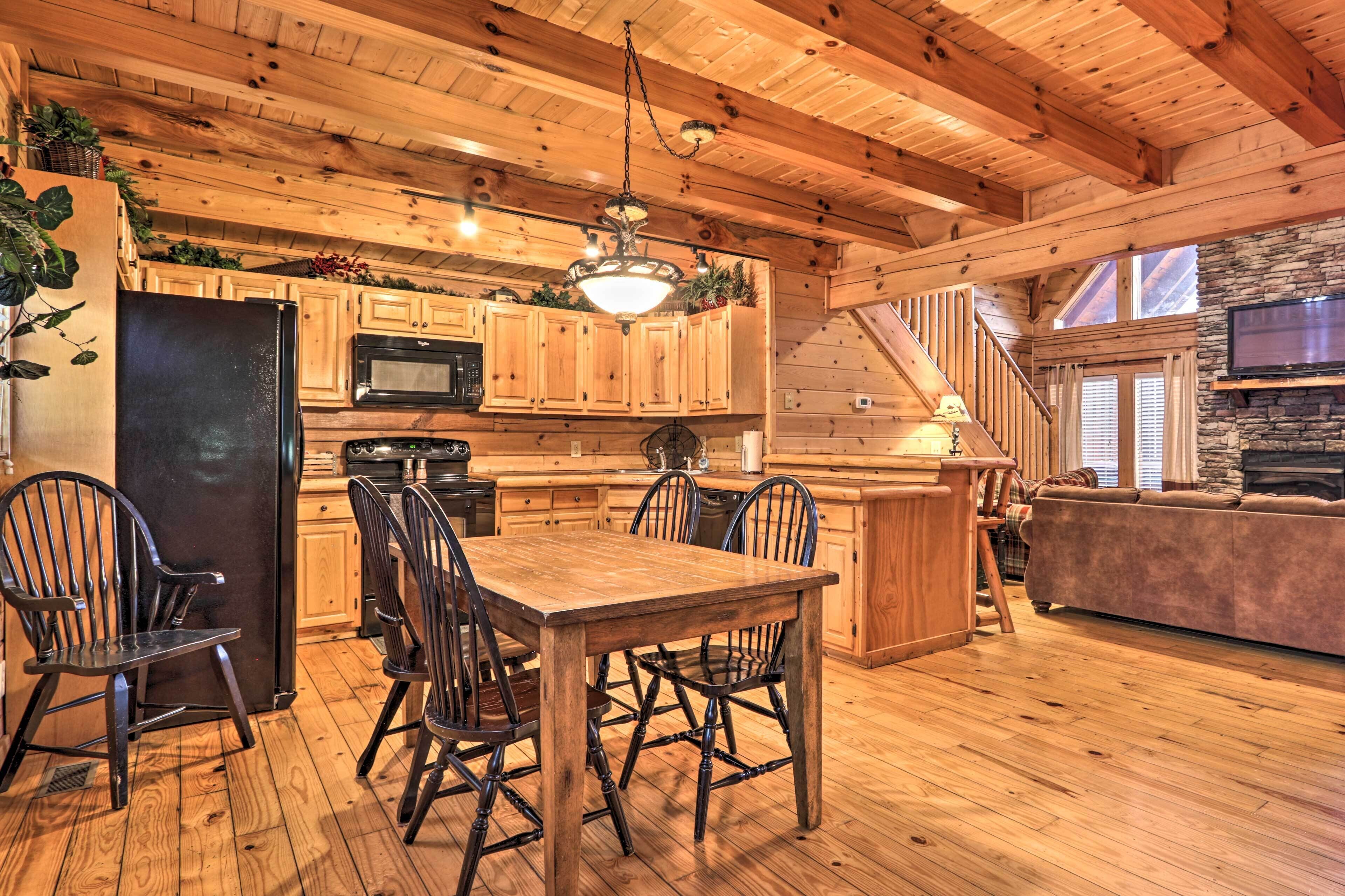 A wooden interior with a dining table, chairs, a refrigerator, a microwave, and a stone fireplace.