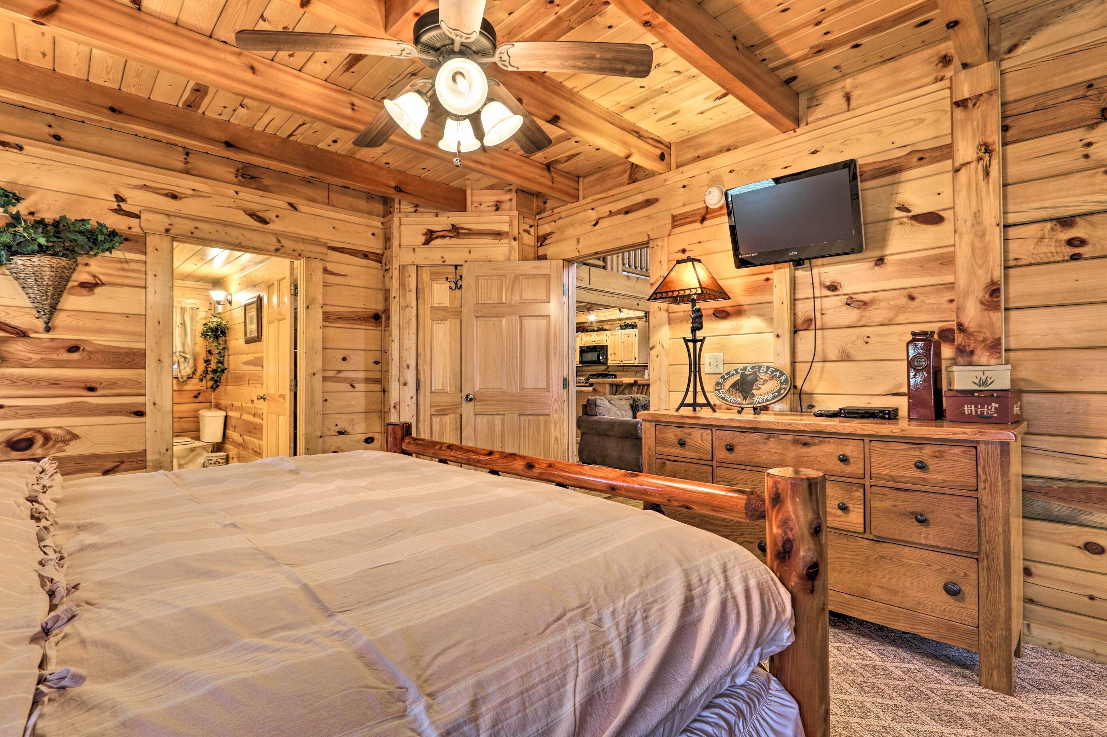 A wooden cabin bedroom with a bed, dresser, TV, and ceiling fan.