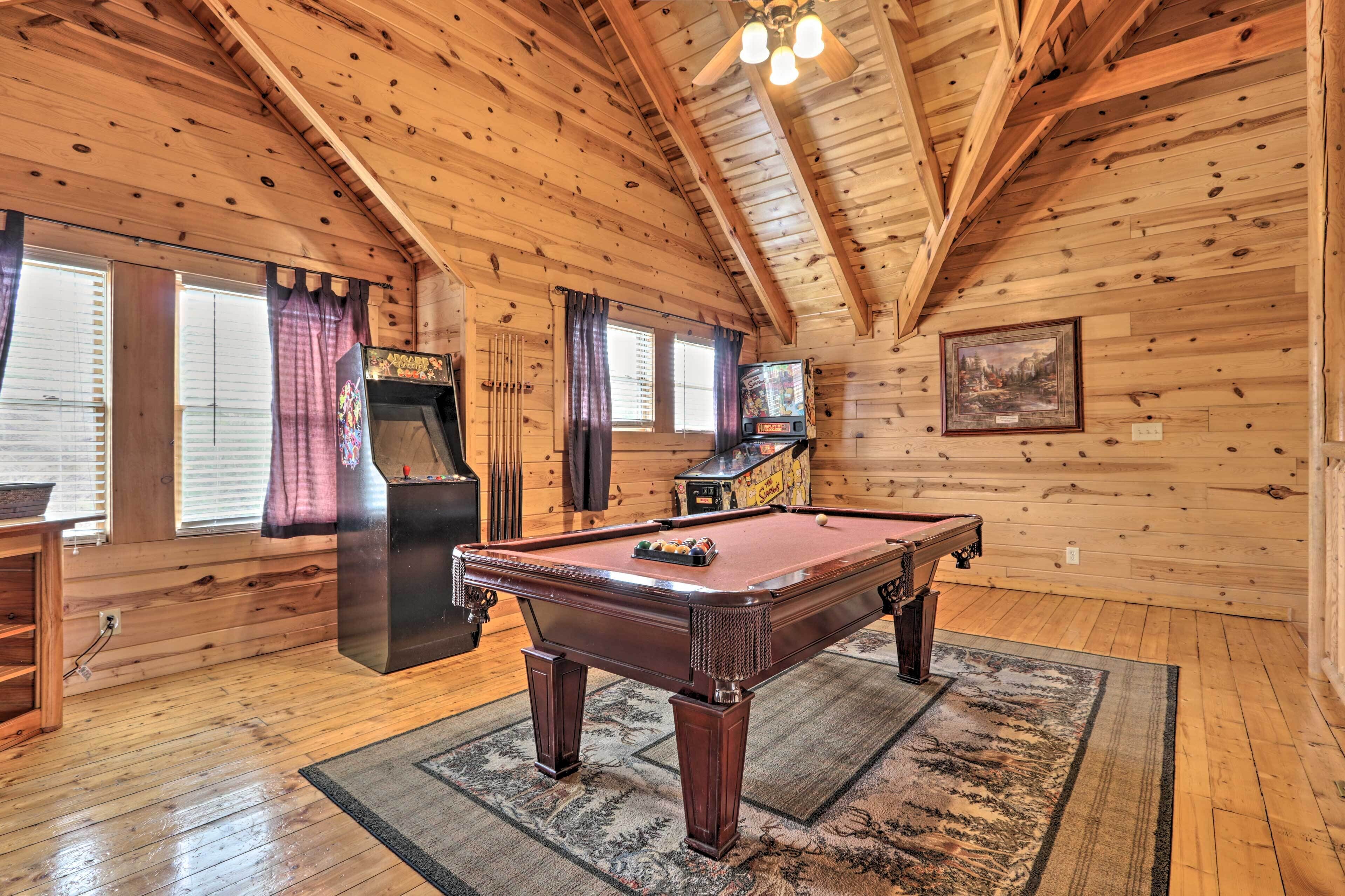 A wooden interior with a pool table, a television, and a pinball machine.