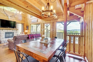 A wooden interior with a fireplace, a dining table, and a television mounted on the wall. - 'mountain Dreams' Cabin: Hot Tub, Sauna & Views! (Sevierville)