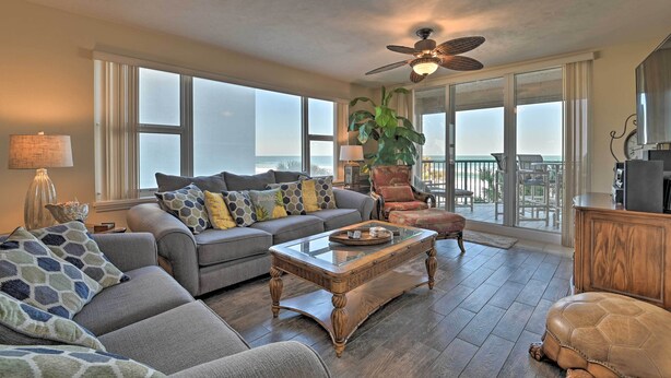 A spacious living room with a large sofa, a coffee table, and a view of the ocean through large windows.