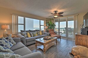 A spacious living room with a large sofa, a coffee table, and a view of the ocean through large windows. - Daytona Beach Seaside Condo w/ Pools & Hot Tubs (Daytona Beach Shores)