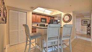 A kitchen with wooden cabinets, a microwave, and a refrigerator. There are two bar stools and a small island with a sink.