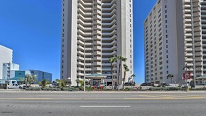 A high-rise hotel with multiple balconies, a parking area, and a clear blue sky.