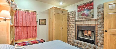 A bedroom with a bed, a wooden wardrobe, a stone fireplace, and a ceiling fan.