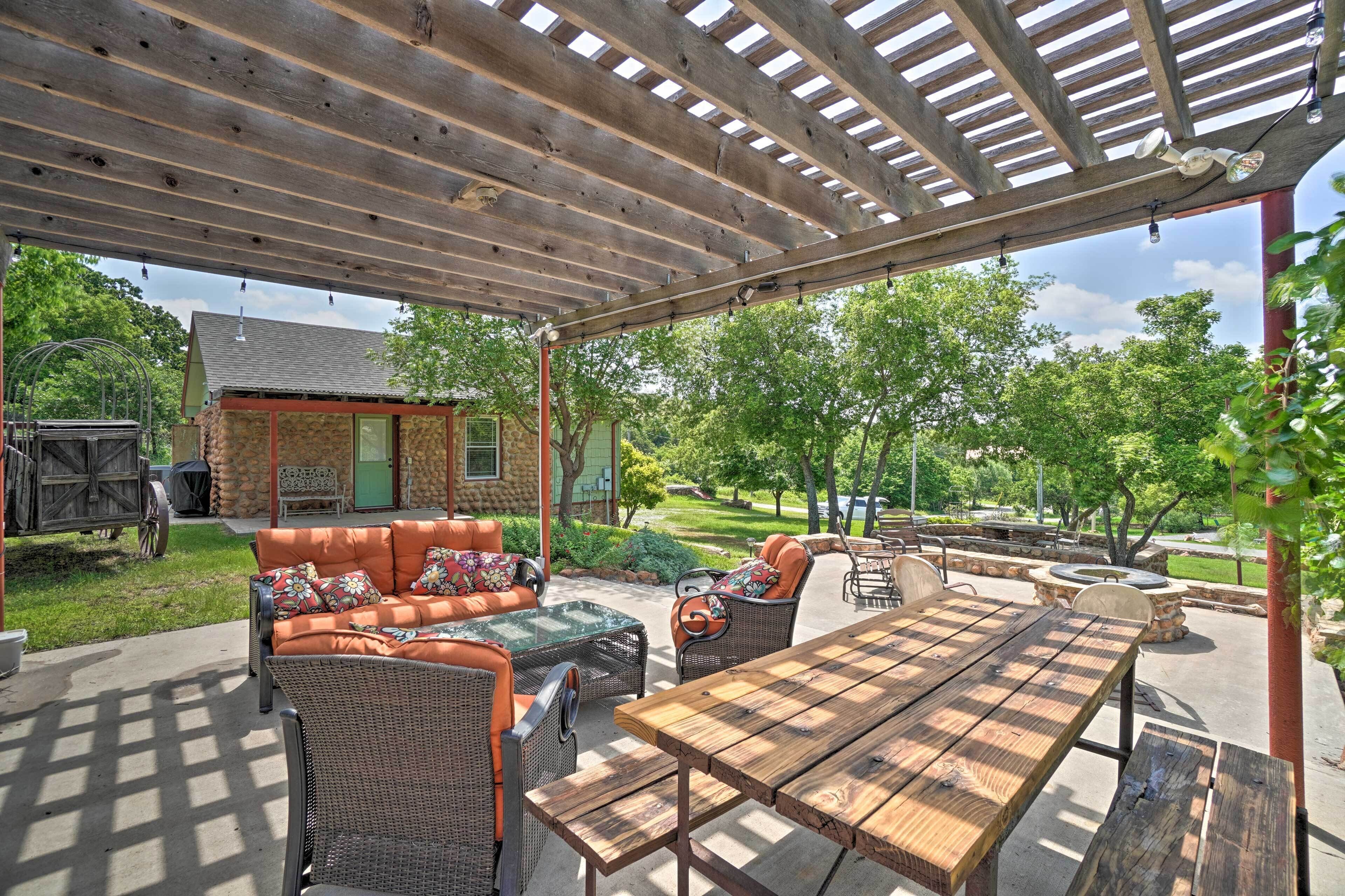 An outdoor patio with a wooden pergola, wicker furniture, and a stone fire pit.