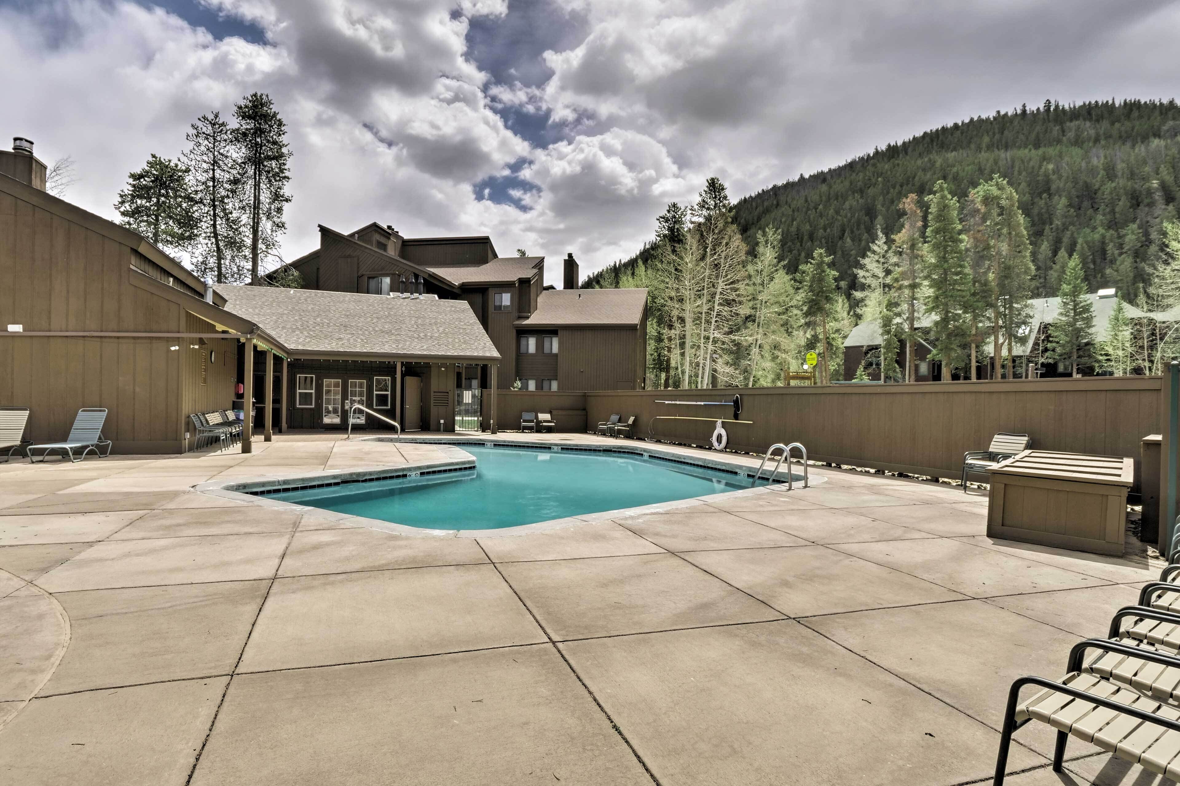 A pool area with lounge chairs, a pool, and buildings in the background.