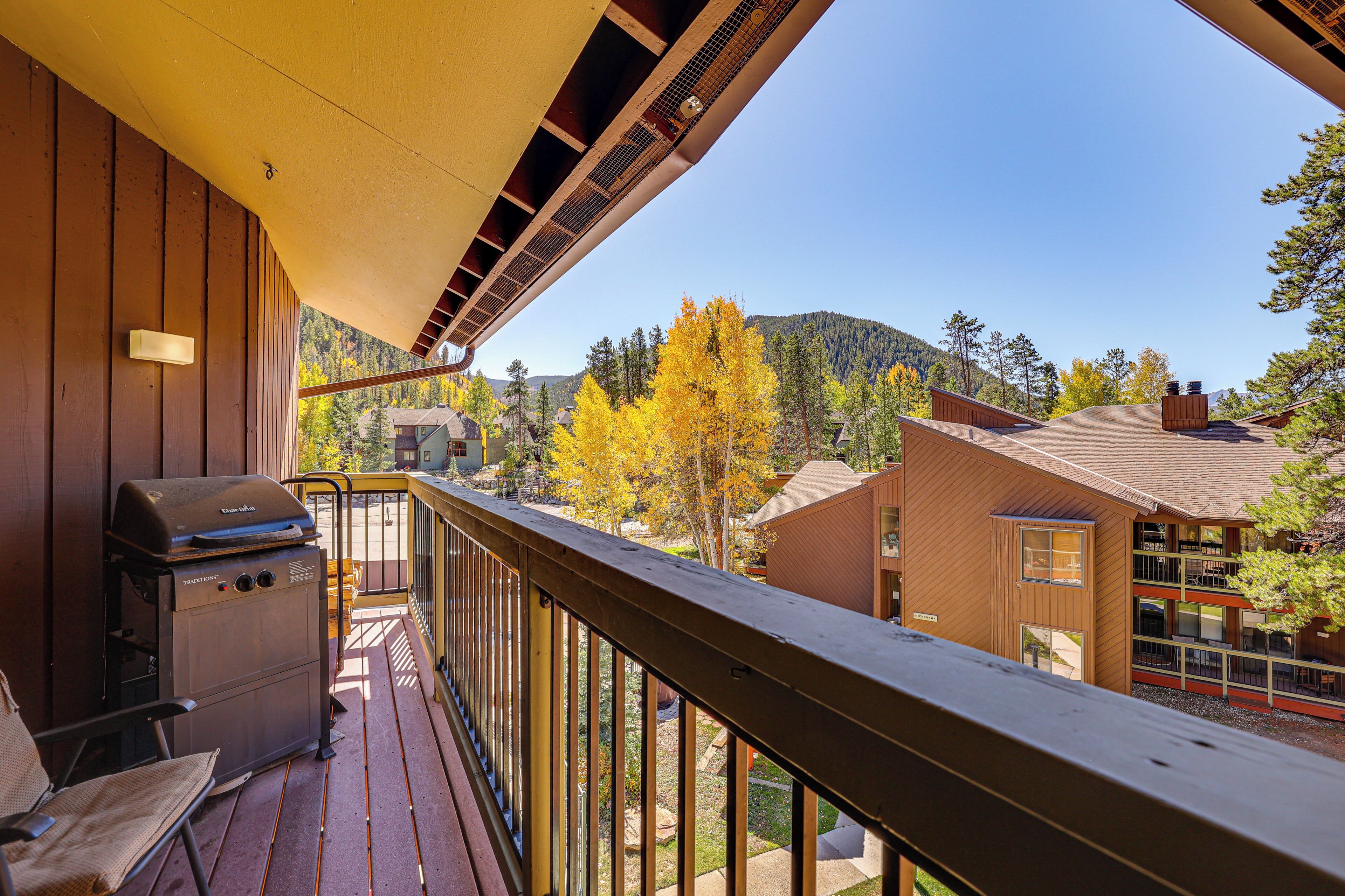 A wooden deck with a grill, a chair, and a view of a mountain and autumn trees.