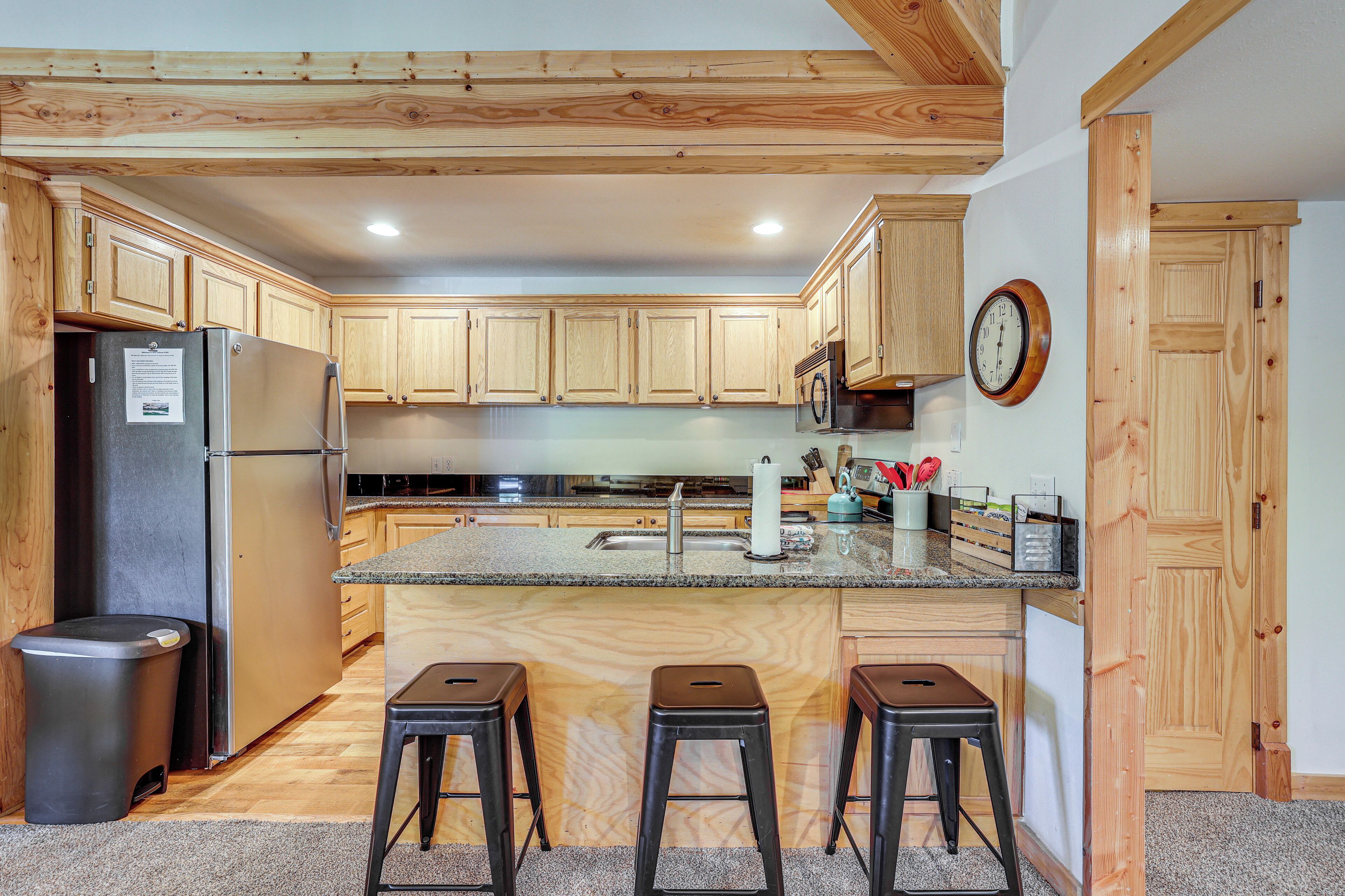 A kitchen with wooden cabinets, a stainless steel refrigerator, a sink, and a clock on the wall.