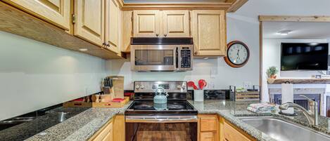 A kitchen with wooden cabinets, a stainless steel microwave, a stove, and a sink.