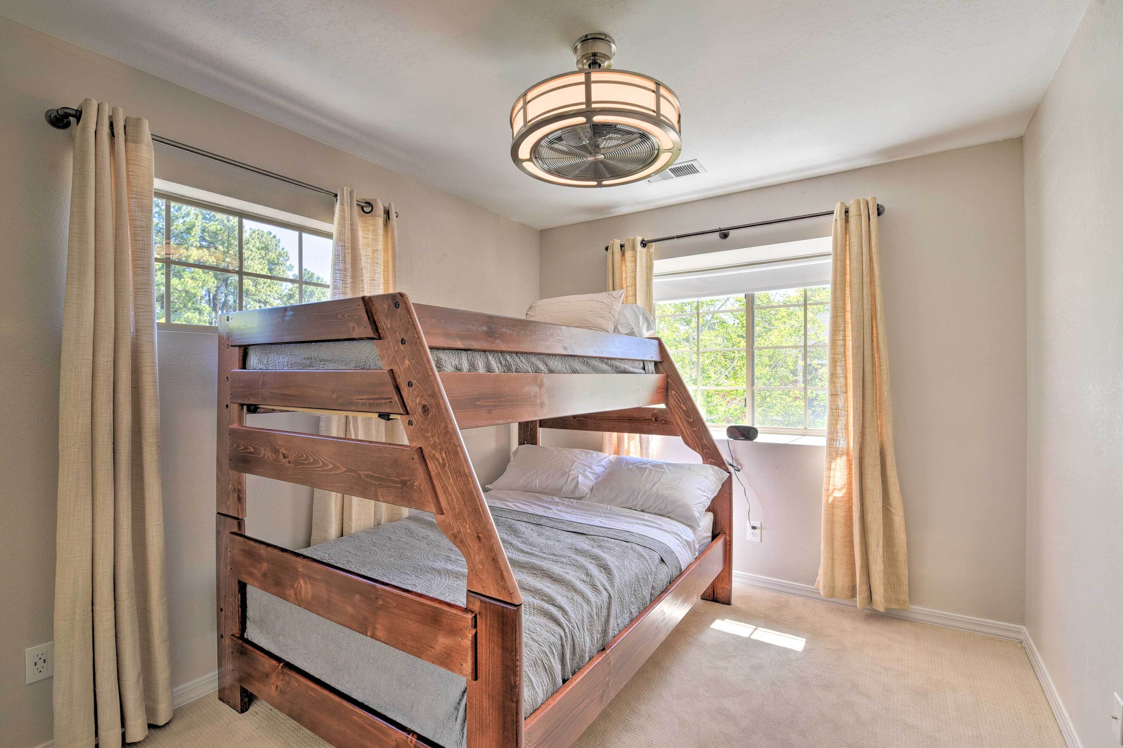 A bunk bed in a room with a ceiling fan, large windows, and beige curtains.
