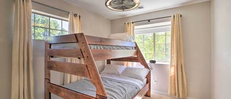 A bunk bed in a room with a ceiling fan, large windows, and beige curtains.