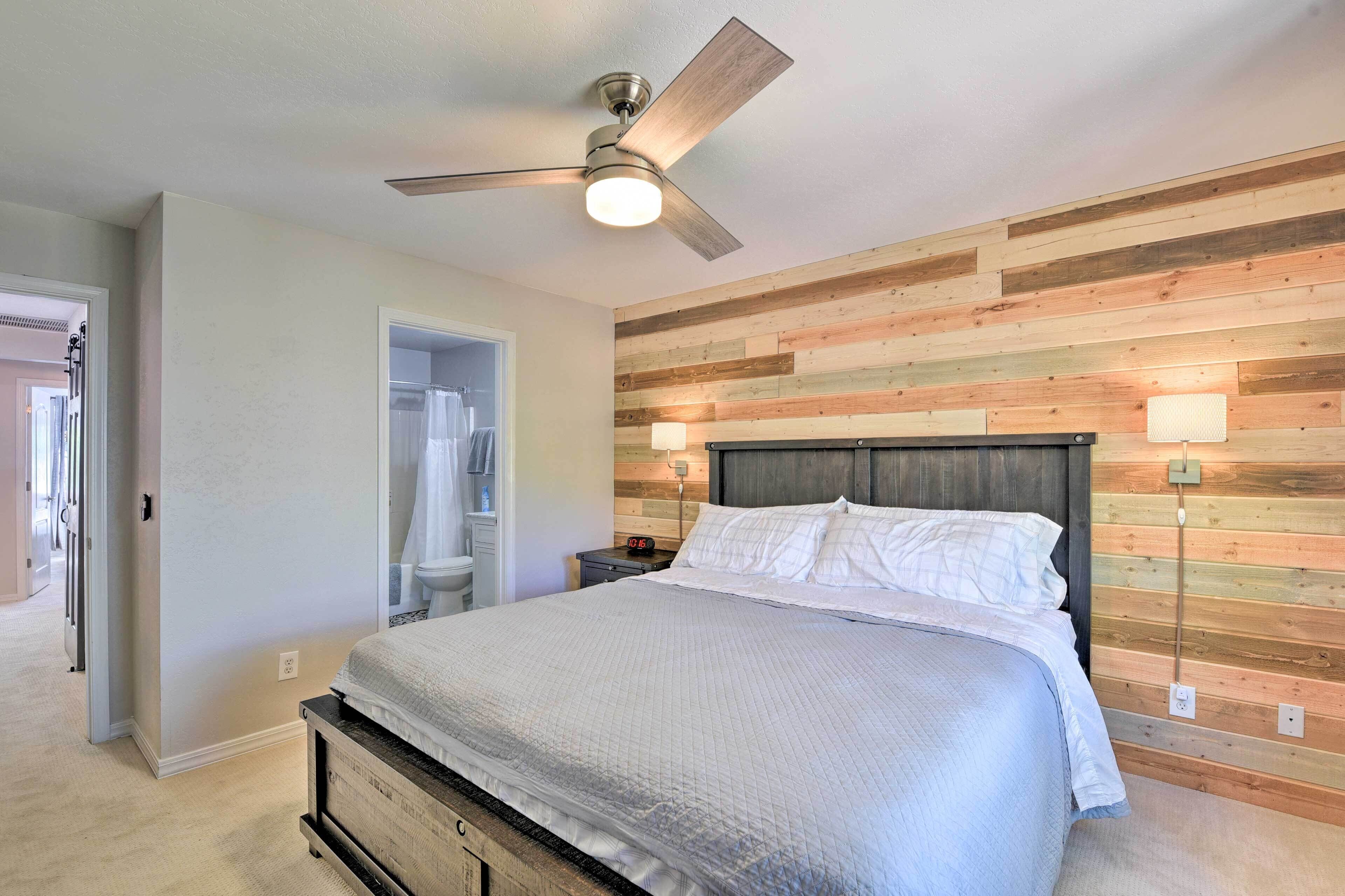 A bedroom with a bed, wooden wall paneling, a ceiling fan, and a nightstand with a lamp.