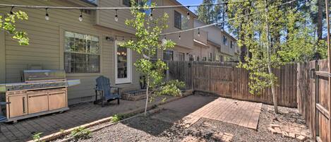 A backyard with a grill, patio furniture, and a wooden fence.