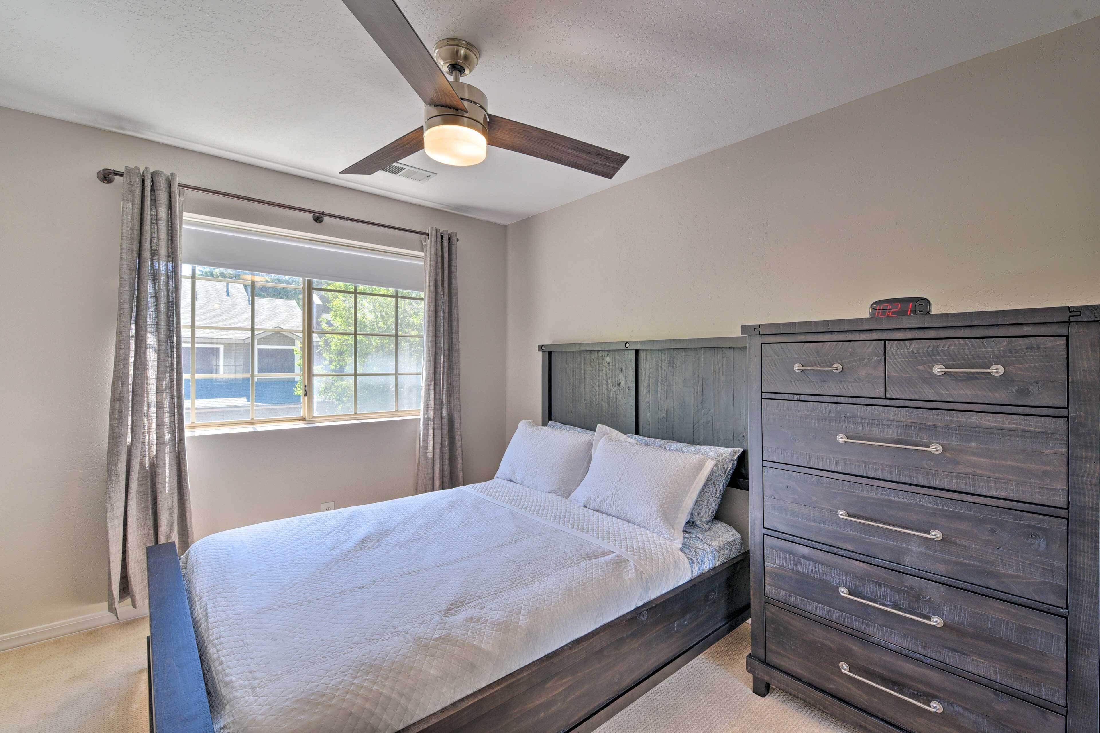 Une chambre à coucher avec un lit, une commode, un ventilateur de plafond et une fenêtre avec des rideaux.