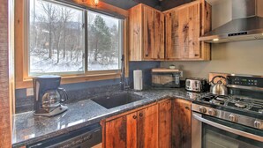 A modern kitchen with wooden cabinets, a stainless steel stove, and a large window with a view of a snowy landscape.