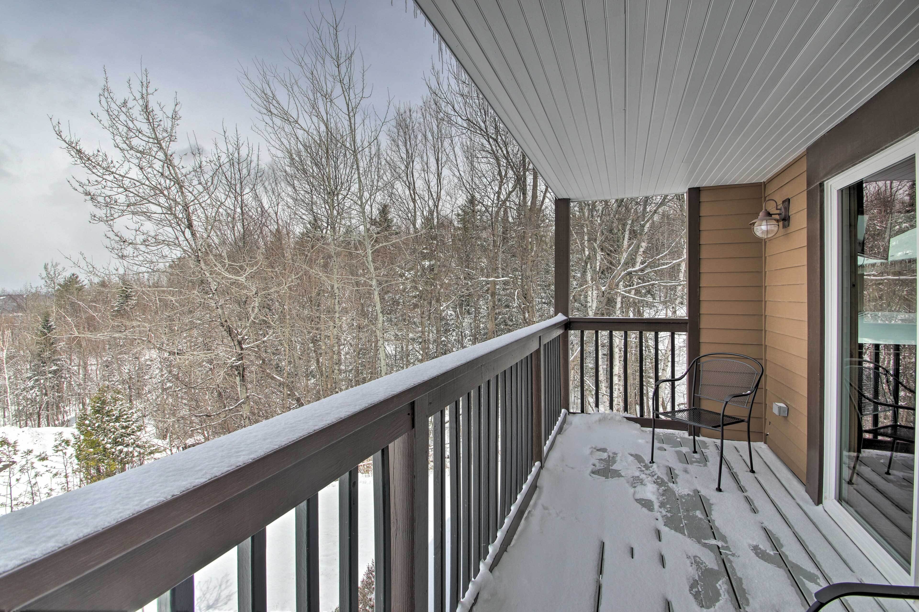 Un balcon doté d’une balustrade en bois, d’une chaise en métal et d’une porte vitrée donnant sur un paysage enneigé.