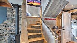 A staircase with wooden steps leading to a room with a stone wall and a wood-burning stove.