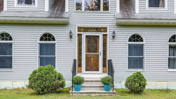 A two-story house with a front door, two potted plants on the steps, and a small lawn. - Upper Valley Retreat on 15 Acres Near Dartmouth (Meriden)