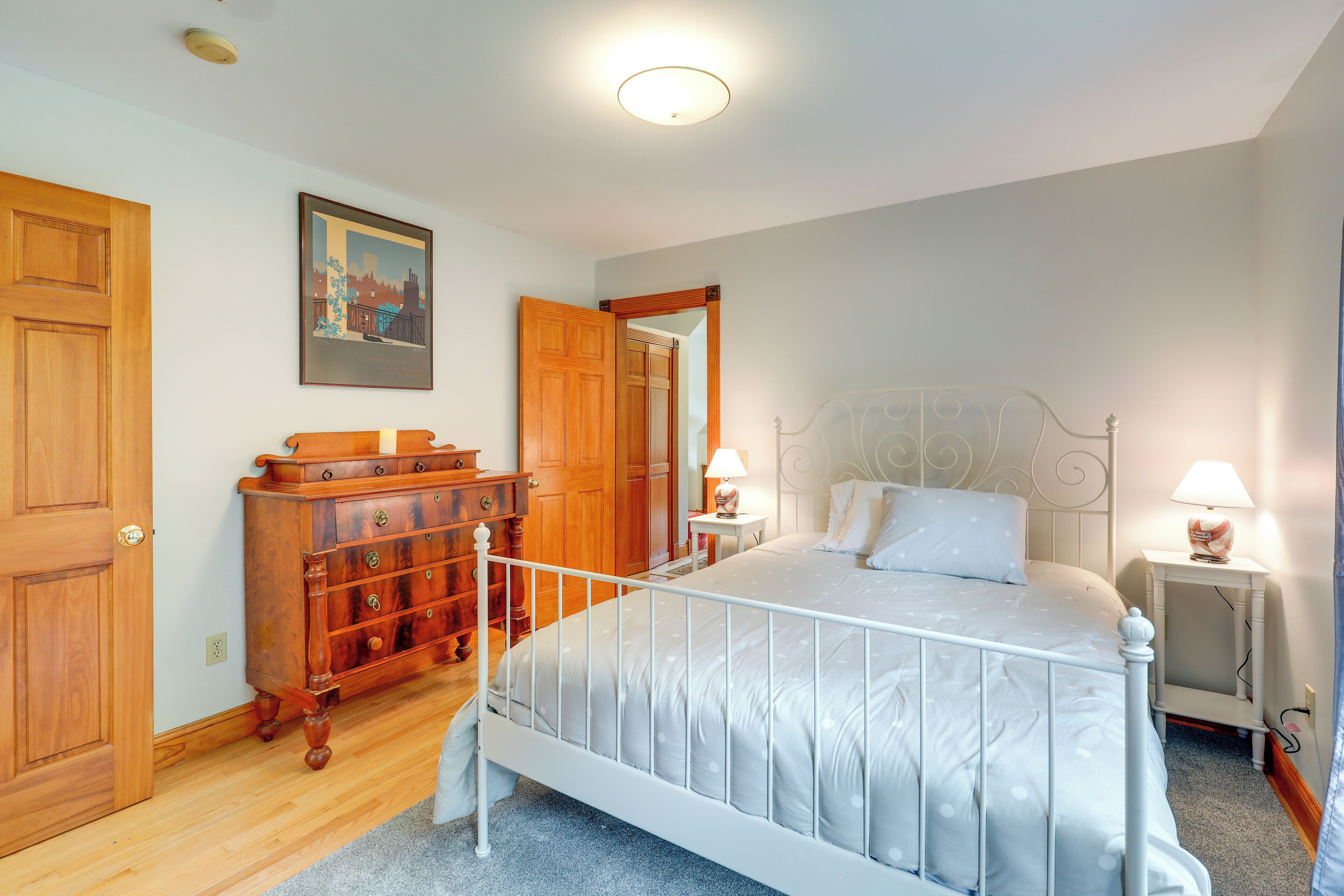 A bedroom with a white metal bed frame, a wooden dresser, and two bedside lamps.