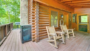 A wooden cabin with a porch, two rocking chairs, a stone wall, and a grill. - Cozy Family Cabin w/ Hot Tub ~ 4 Mi to Dollywood! (Pigeon Forge)