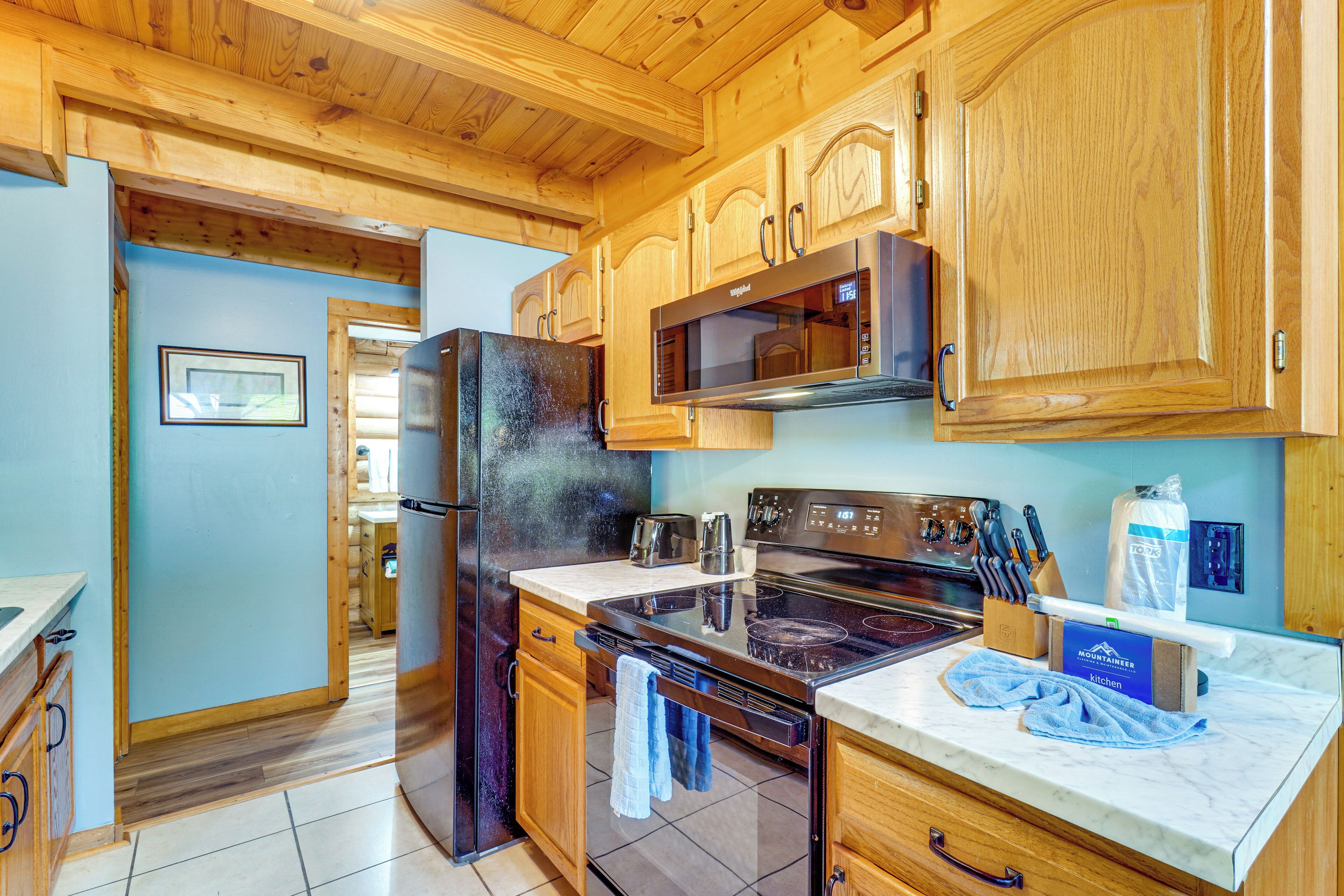 A kitchen with wooden cabinets, a refrigerator, an oven, a microwave, and a countertop with a box of paper towels.