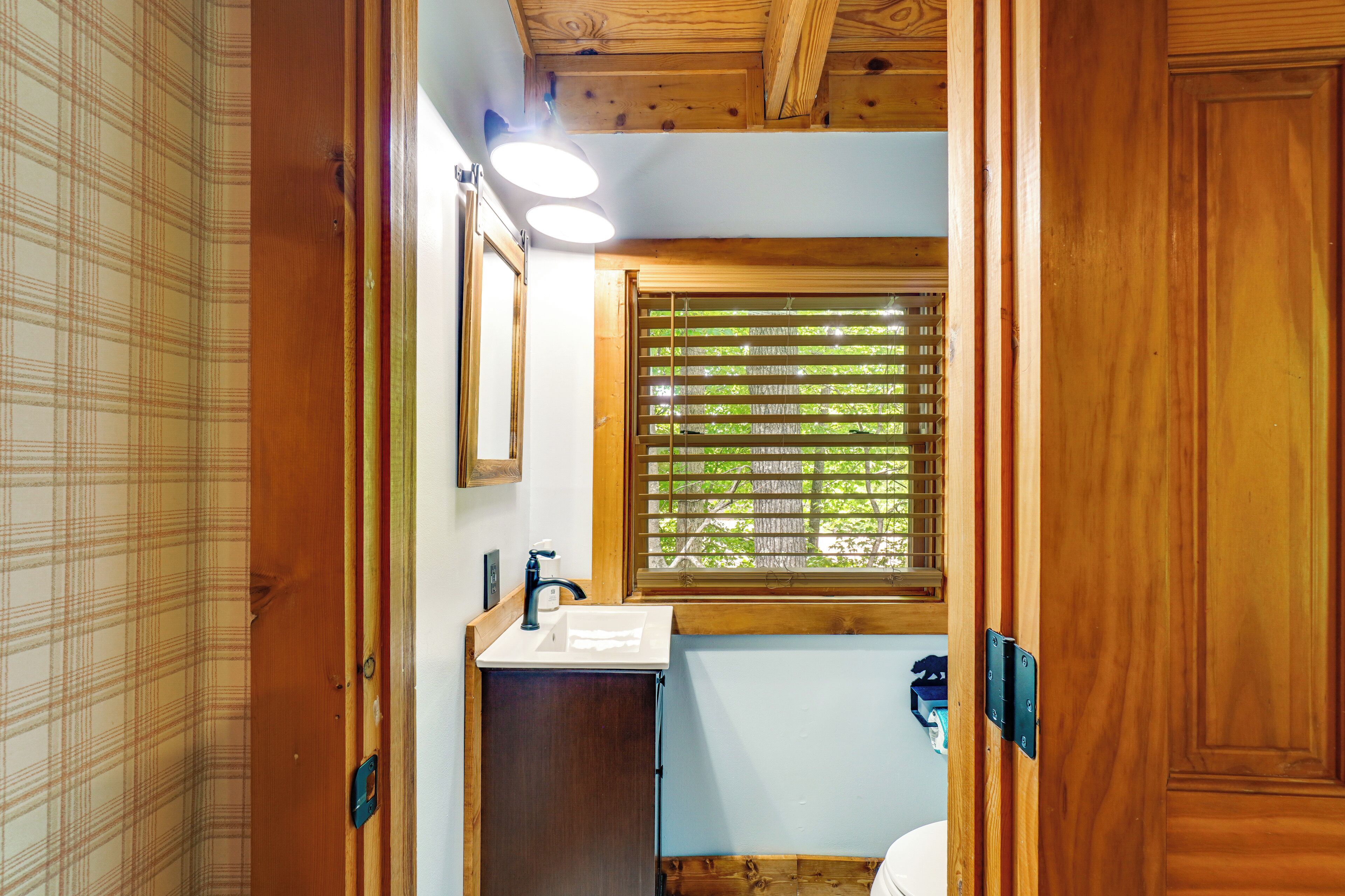 Un baño con tocador de madera, un lavabo, un espejo y una ventana con persianas.