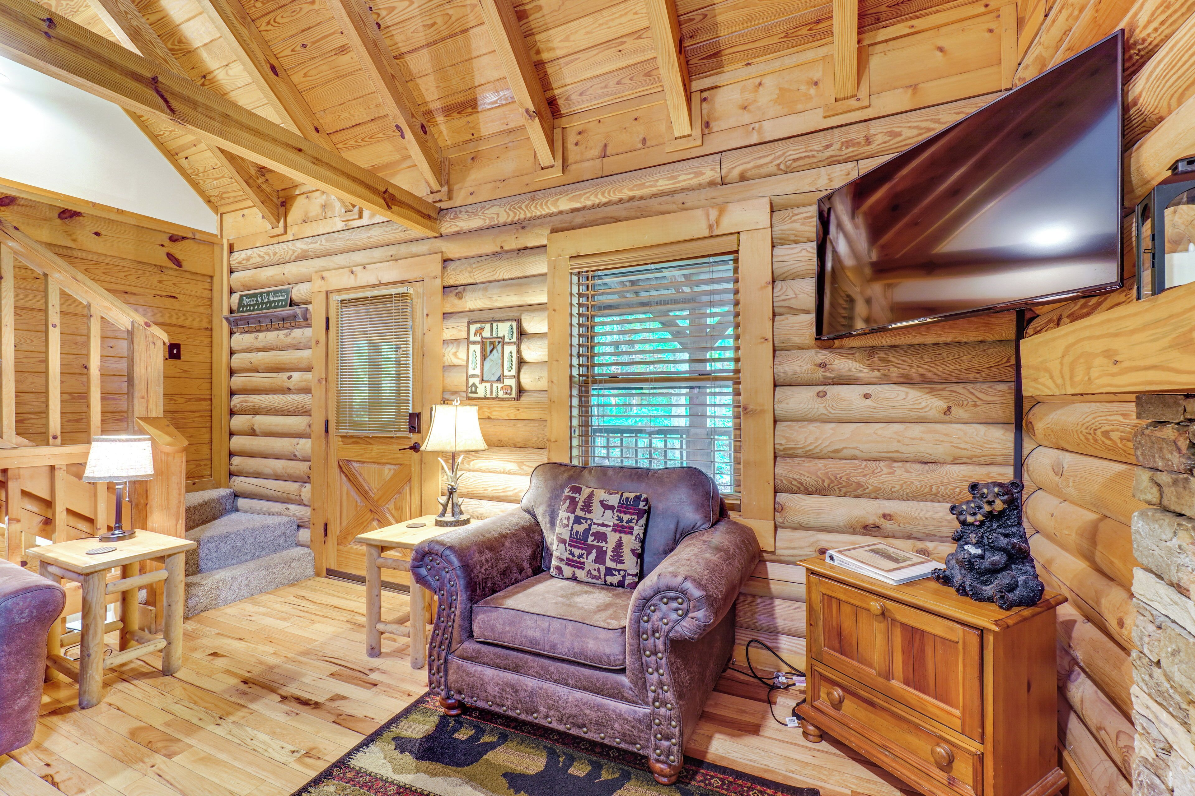 A log cabin interior with a leather armchair, a TV mounted on the wall, and a wooden cabinet with a bear figurine.