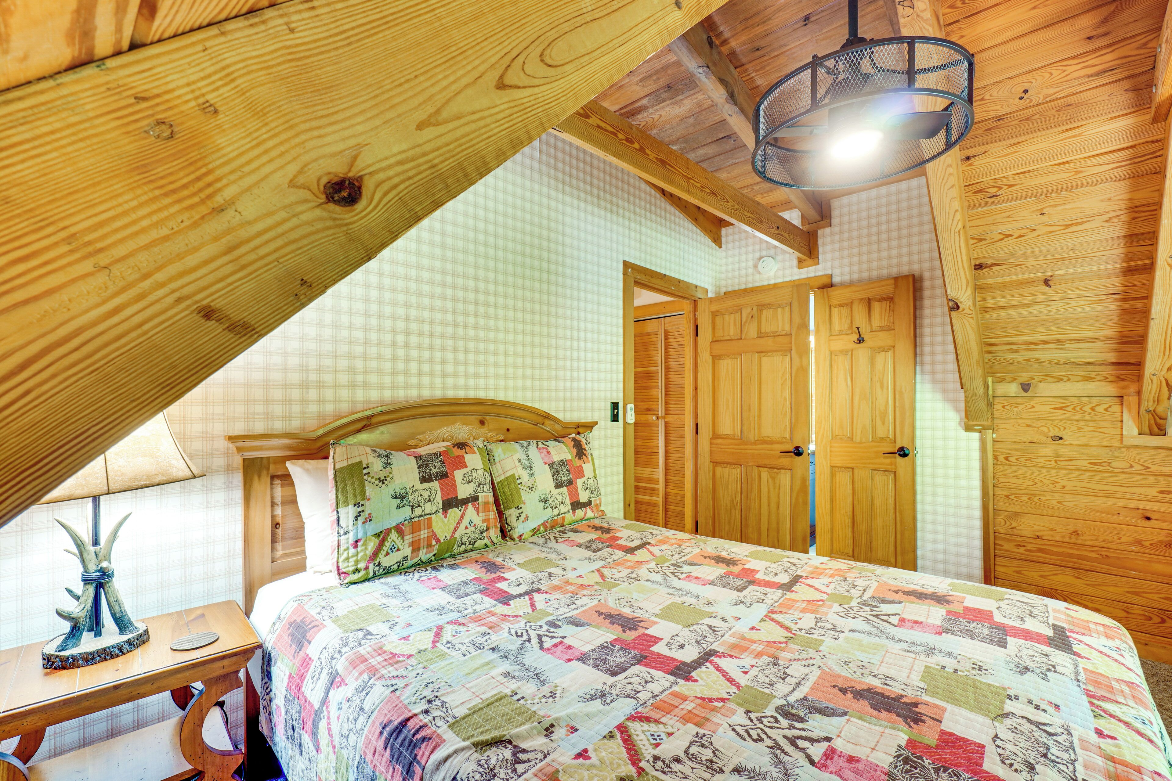 Een slaapkamer met een houten plafond, een gewatteerde spreideken, een nachtkastje en een lamp.