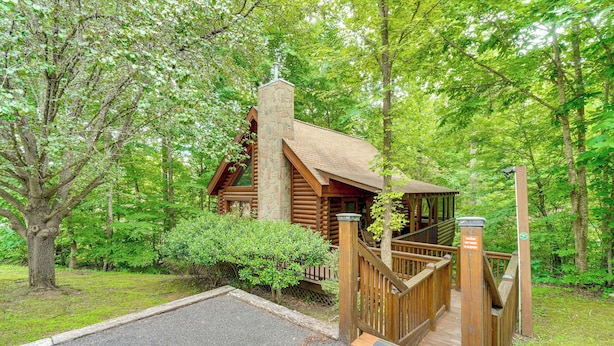 A log cabin with a stone chimney, wooden deck, and a gated entrance. - Cozy Family Cabin w/ Hot Tub ~ 4 Mi to Dollywood! (Pigeon Forge)
