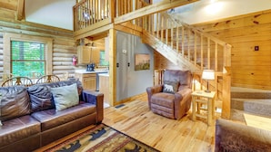 A log cabin interior with a wooden staircase, a sofa, a chair, and a dining area. - Cozy Family Cabin w/ Hot Tub ~ 4 Mi to Dollywood! (Pigeon Forge)