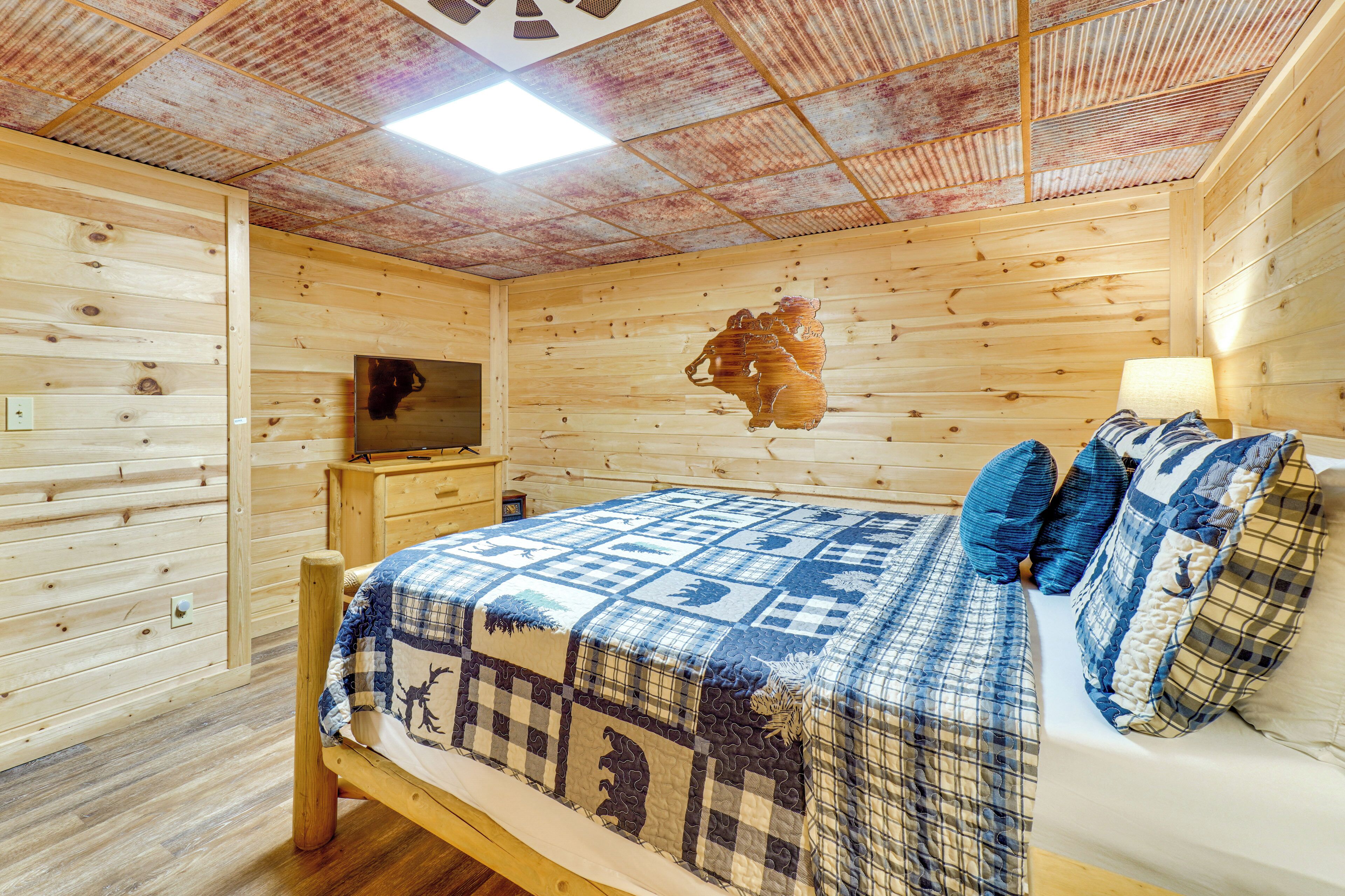 Habitación de cabaña de madera con cama, cómoda de madera, cabeza de animal montada y ventilador de techo.