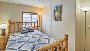 A bedroom with a wooden bed frame, a quilt, a window with a view, a painting on the wall, and a lamp. - Columbia Falls Home ~ 22 Mi to Glacier Natl Park! (Columbia Falls)
