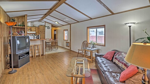 A spacious living area with a wooden floor, a leather sofa, a glass coffee table, a television, and a dining area with wooden furniture. - Columbia Falls Home ~ 22 Mi to Glacier Natl Park! (Columbia Falls)