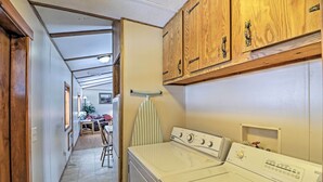 A laundry room with a washer and dryer, wooden cabinets, and a striped ironing board. - Columbia Falls Home ~ 22 Mi to Glacier Natl Park! (Columbia Falls)