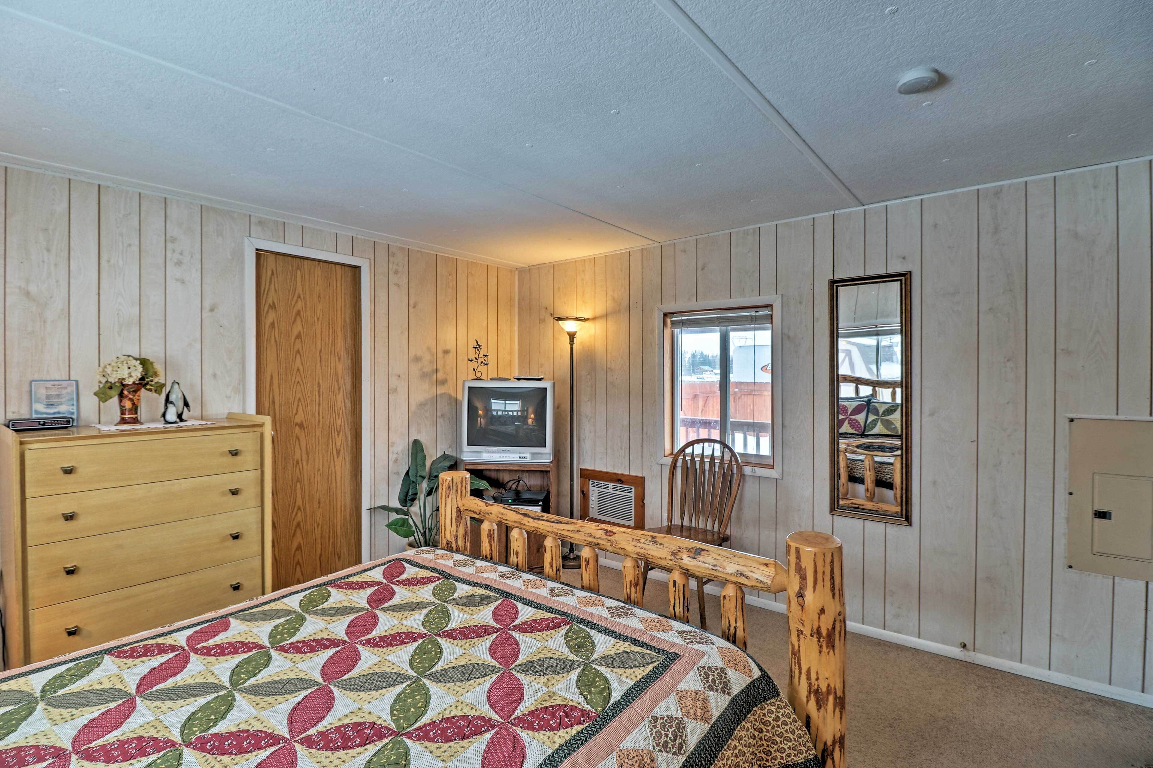 Une chambre à coucher avec un lit en bois, une commode, un téléviseur et une fenêtre donnant sur un beau paysage.