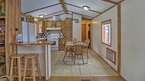 A compact kitchen with wooden cabinets, a central island with stools, and a dining table with chairs. - Columbia Falls Home ~ 22 Mi to Glacier Natl Park! (Columbia Falls)