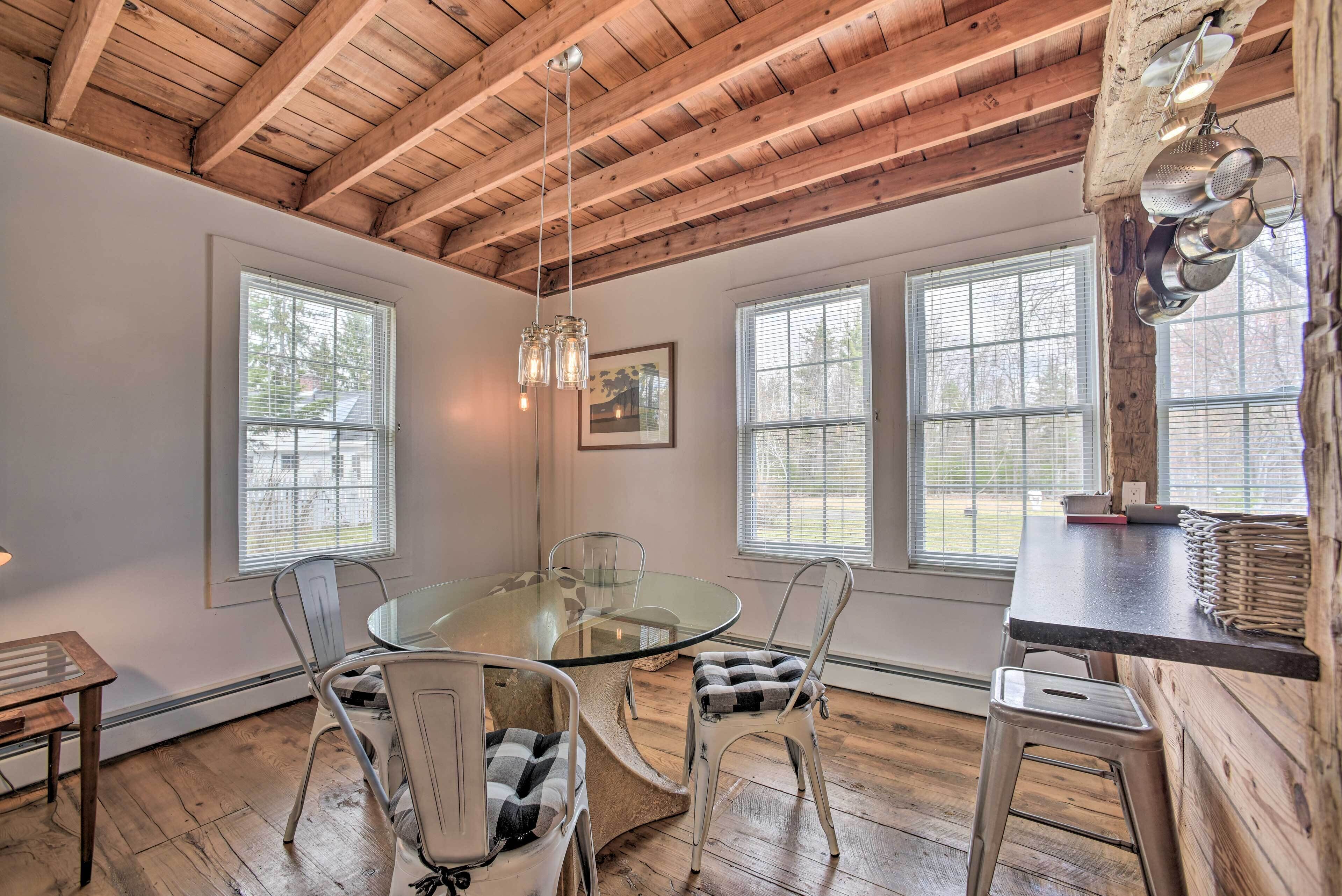 A dining area with a glass table surrounded by metal chairs, wooden floors, and a wooden ceiling.