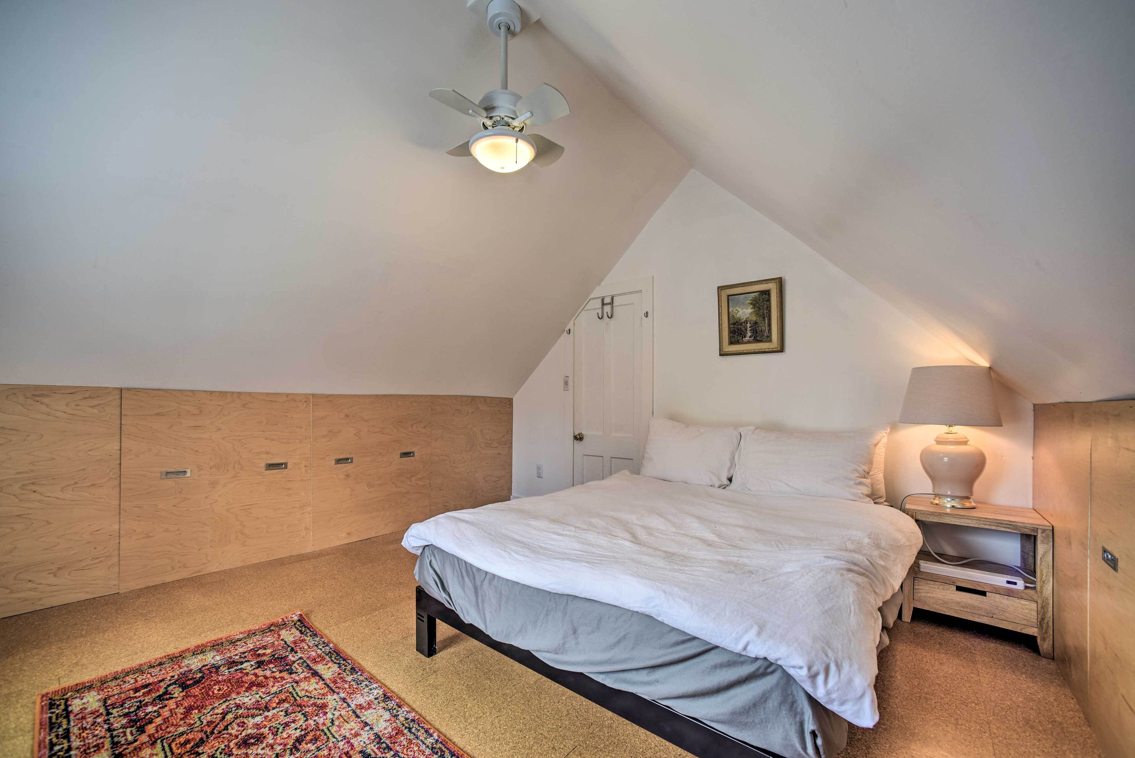 Un dormitorio con cama, mesita de noche, lámpara, ventilador de techo, puerta y alfombra.