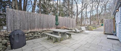 Un patio con baldosas de piedra, una valla de madera y una zona de parrilla cubierta.