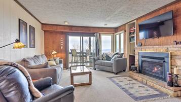 A living room with a fireplace, a television mounted on the wall, and a large window with a view.