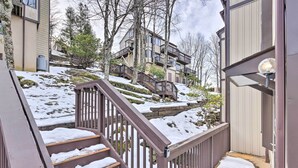 Un edificio residenziale con una scala in legno che conduce a un patio, circondato da terreno e alberi coperti di neve.