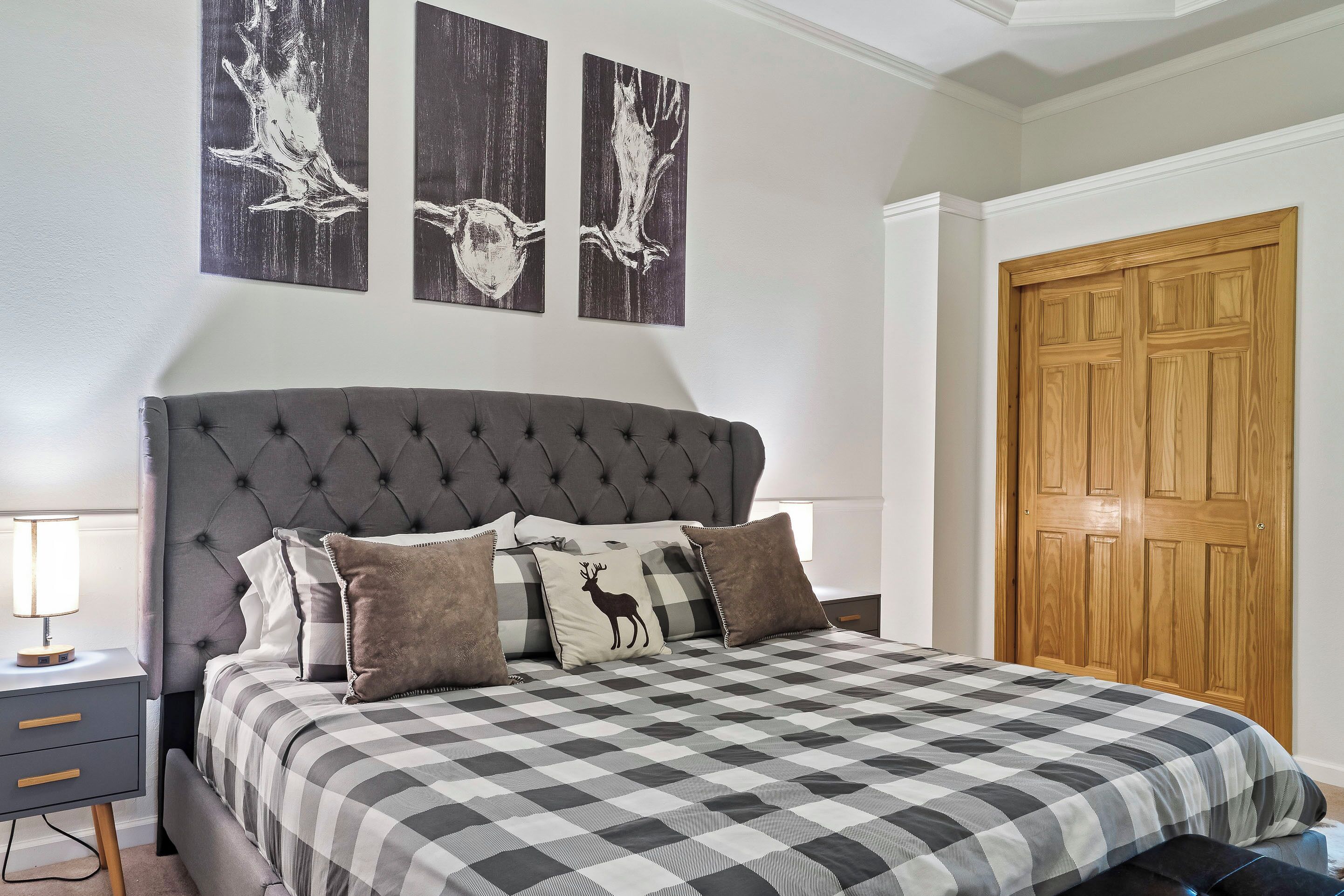 Une chambre à coucher avec une tête de lit capitonnée, une couvre-lit à carreaux et une table de chevet avec une lampe.