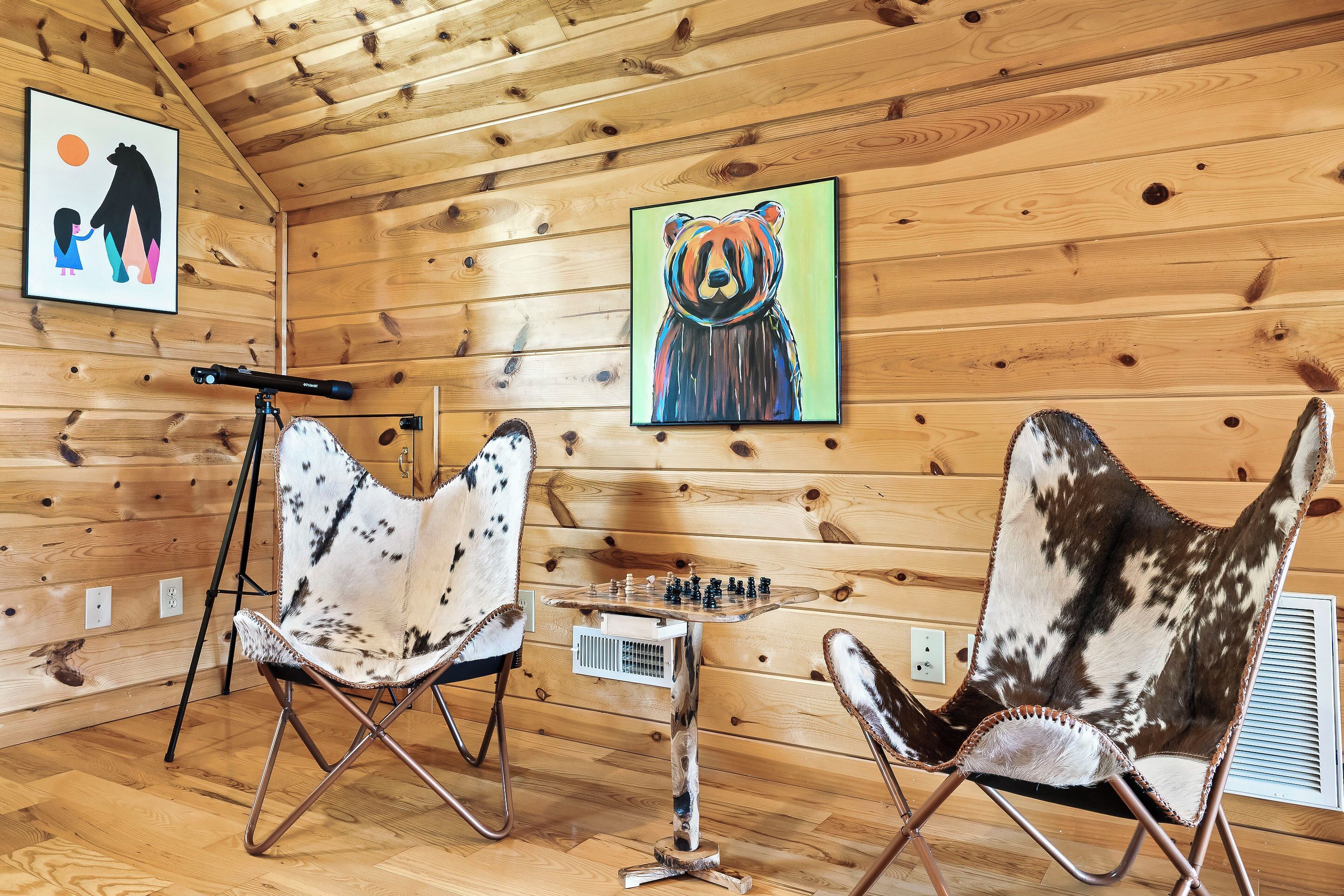 L’intérieur d’un chalet chaleureux, avec des murs en bois, une table d’échecs et deux fauteuils à motifs.