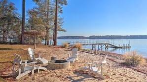 Un décor de plage avec des fauteuils Adirondack, un foyer et une jetée qui s’avance dans un lac.