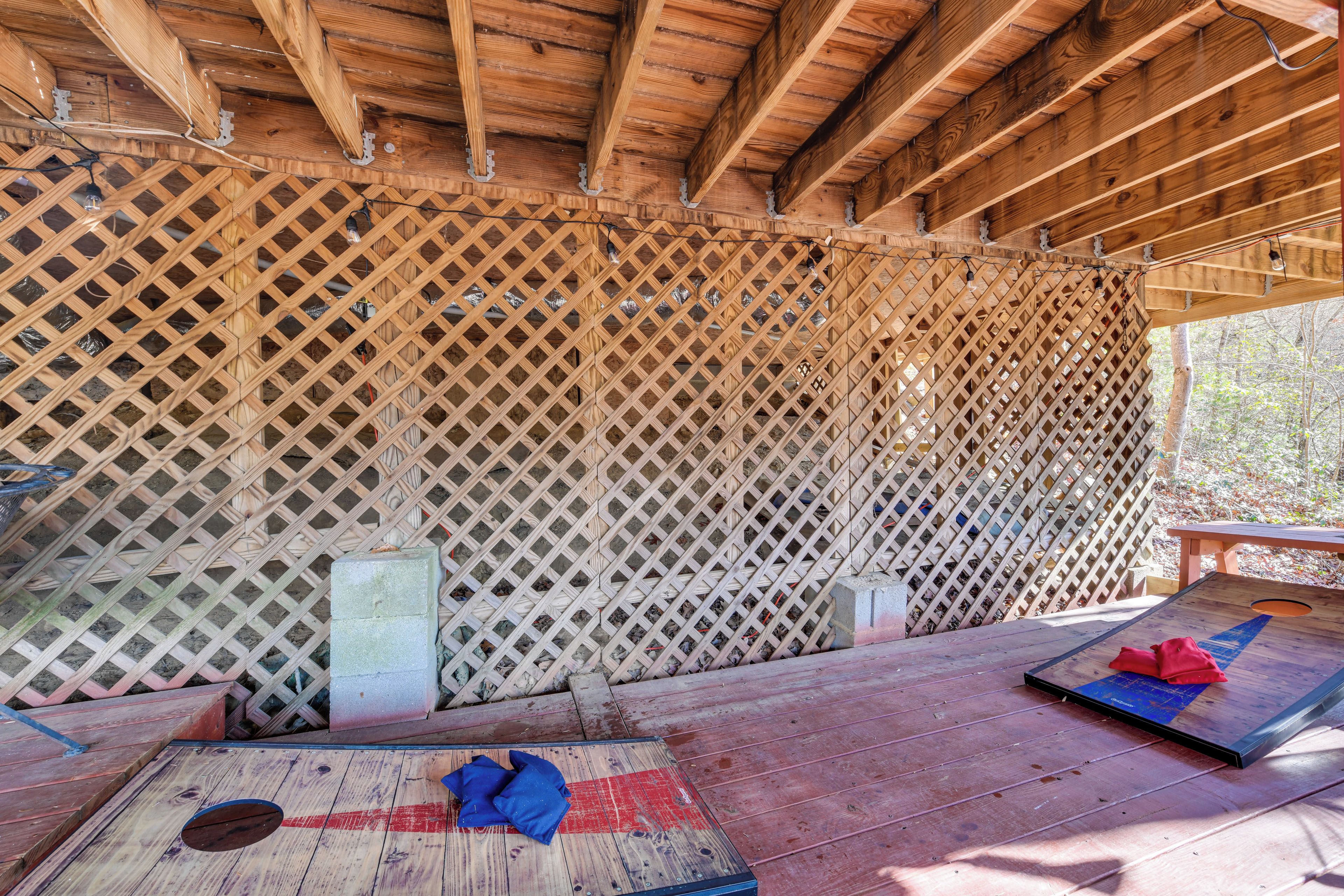A covered wooden deck with a lattice wall, a table, and a mat with a red cloth.
