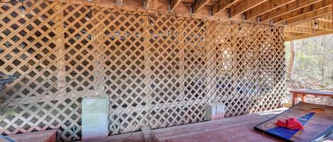 A covered wooden deck with a lattice wall, a table, and a mat with a red cloth.